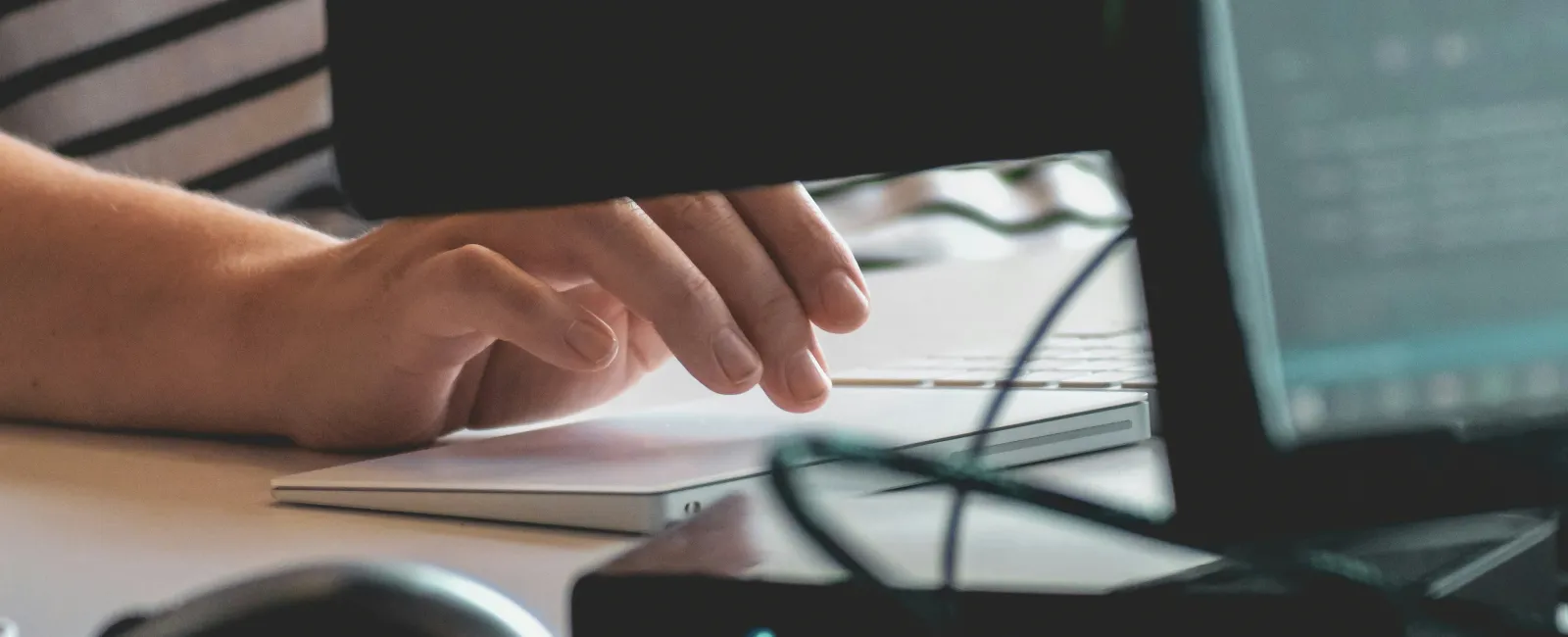 Person typing on a white keyboard at a desk with computer monitors and a mouse nearby