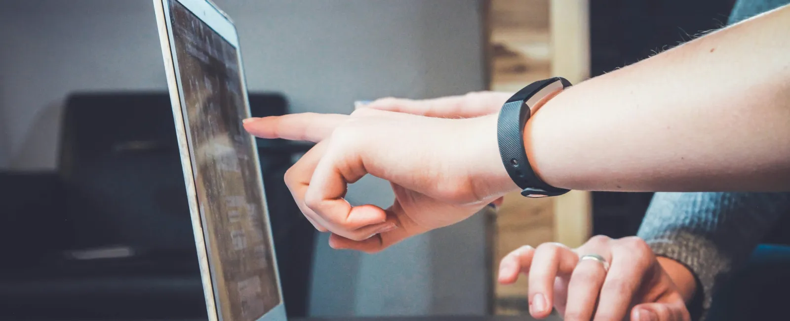 Person pointing at a laptop screen while another types on the keyboard during a collaborative work session.