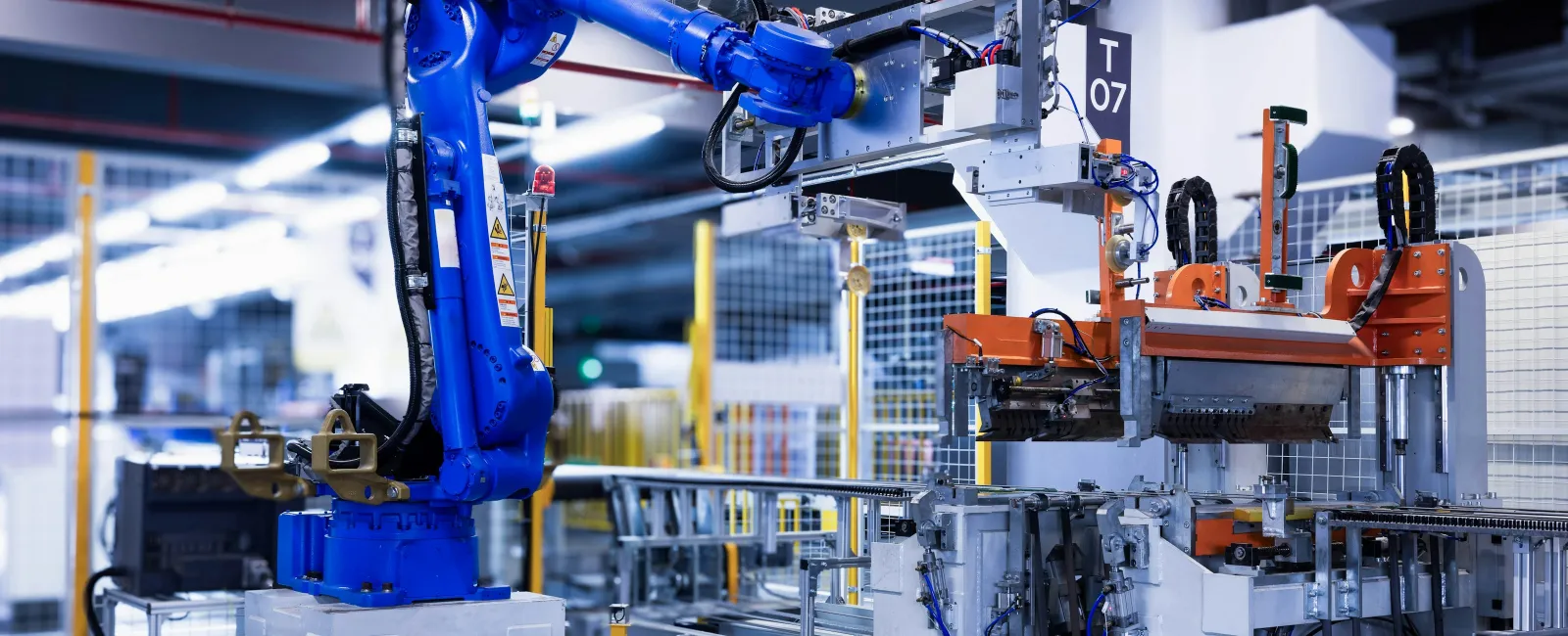 Blue industrial robotic arm operating machinery in a modern automated factory setting with metal framework and equipment.