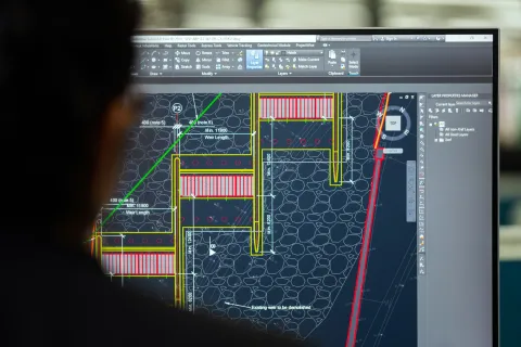 Architect reviewing detailed digital engineering plan with measurements and structural elements on computer screen.