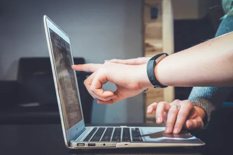 Close-up of two people collaborating on a laptop, one pointing at the screen and another typing.